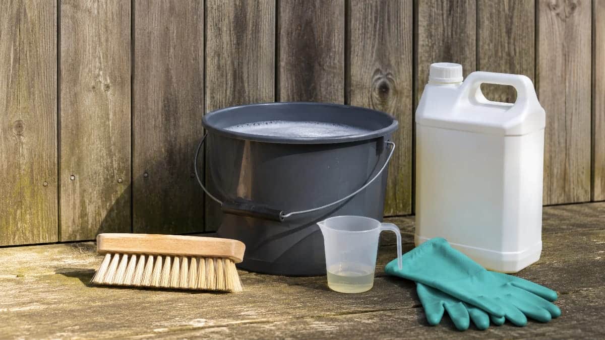 Brosse souple, savon noir, doseur et nettoyant bois concentré devant un bardage extérieur